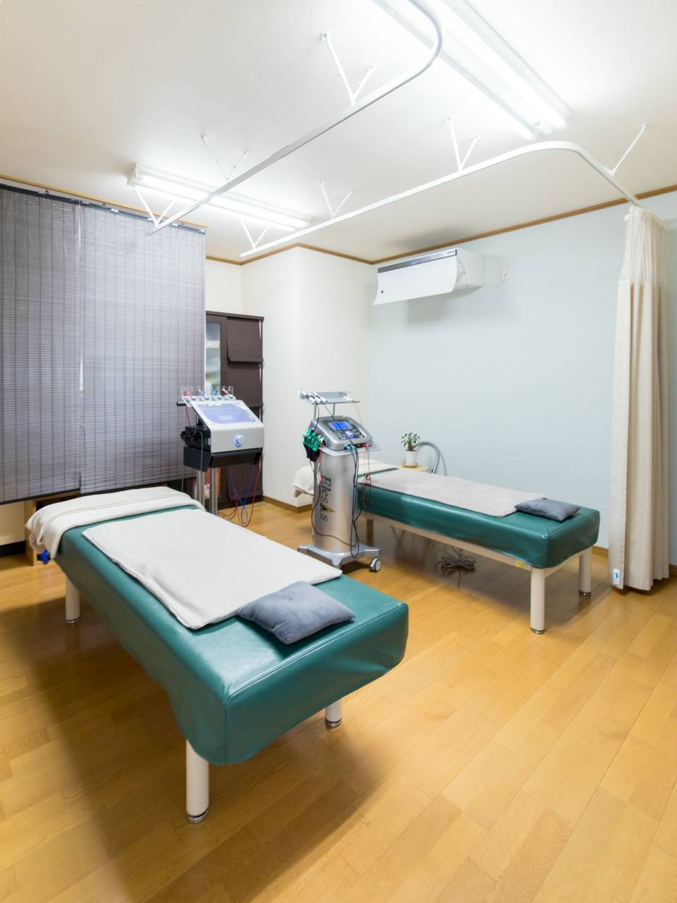 木の床と緑のベッドがある、ゆうぷらすの明るい施術室